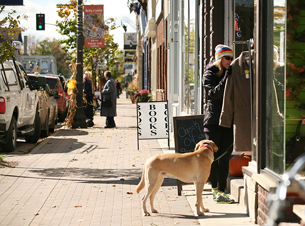 A shopper with her dog take a look at a coat on a rack on the sidewalk of a town street.